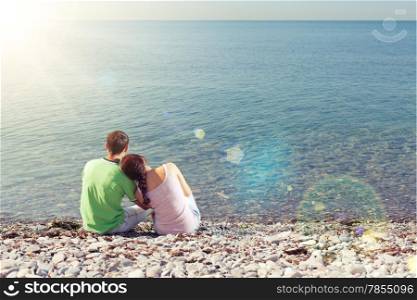 Young lovers sitting near water, looking over horizon and dreaming, sunbeams and lens flares