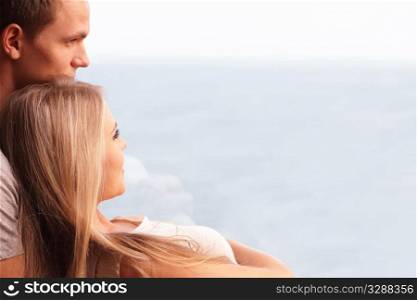 Young loving couple embracing and looking at a beautiful seaview in the window