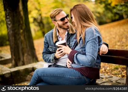 Young loving couple on a bench in autumn park and holding coffee to go in the hands