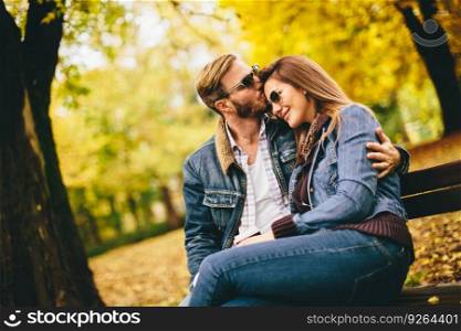 Young loving couple on a bench in autumn park and holding coffee to go in the hands