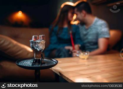 Young loving couple relax and smoking hookah, tobacco smoke at night bar. Young couple relax and smoking hookah