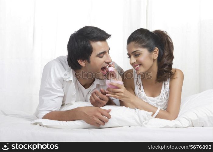 Young loving woman feeding man ice-cream in bed
