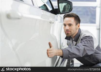 Young maintenance engineer examining car in repair shop