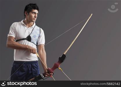 Young male archer holding bow and arrow isolated over gray background