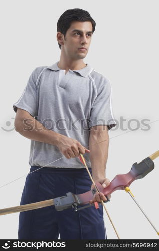 Young male archer holding bow and arrow isolated over gray background