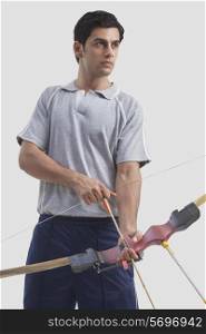 Young male archer holding bow and arrow isolated over gray background