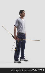 Young male archer standing with bow and arrow isolated over gray background