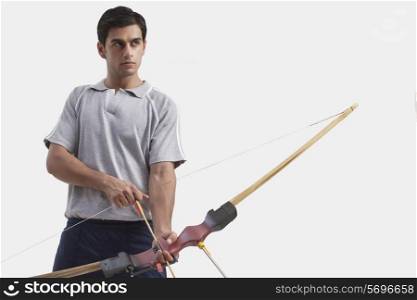 Young male archer with bow and arrow against gray background