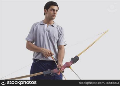 Young male archer with bow and arrow isolated over gray background