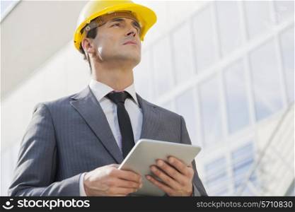 Young male architect holding tablet PC against building
