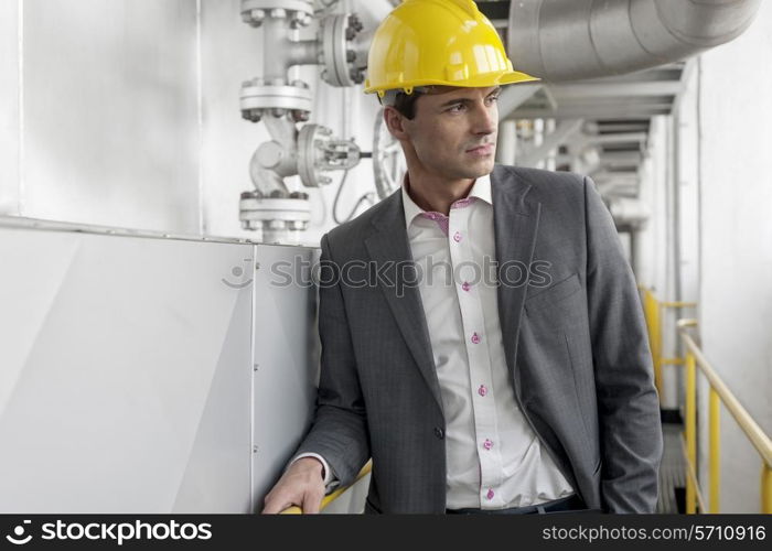 Young male architect in hard hat looking away at industry