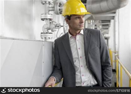 Young male architect in hard hat looking away at industry