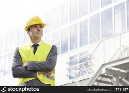 Young male architect in protective wear standing arms crossed outside building