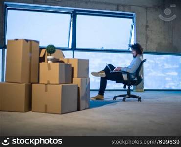 young male architect on construction site checking documents and business workflow using laptop computer with cardboard boxes around him in new startup office