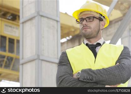 Young male architect standing arms crossed at construction site