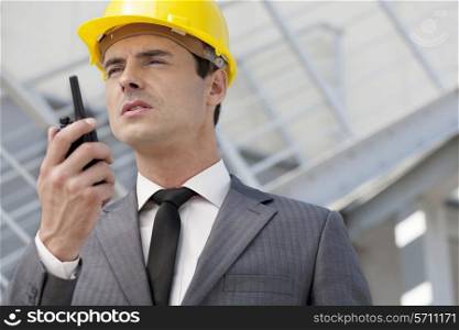 Young male architect talking on two-way radio outdoors