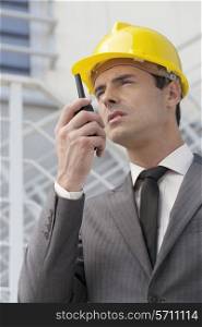 Young male architect talking on walkie-talkie against building