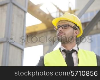Young male architect wearing hard hat looking away at construction site