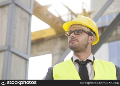 Young male architect wearing hard hat looking away at construction site