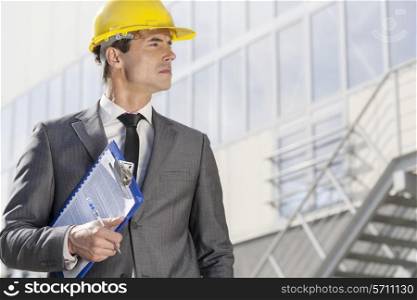 Young male architect with clipboard looking away outside office building