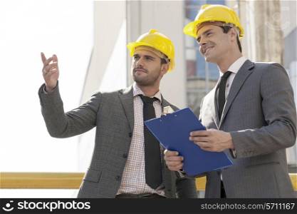 Young male architects with clipboard discussing at construction site