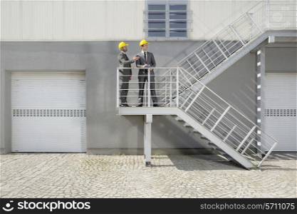 Young male architects with clipboard discussing on stairway