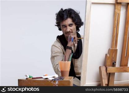 Young male artist looking at painting against colored background