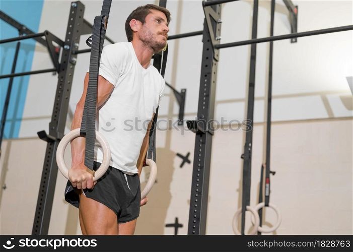 Young Male Athlete exercising With Gymnastic Rings In The Gym. High quality photo.. Young Male Athlete exercising With Gymnastic Rings In The Gym.