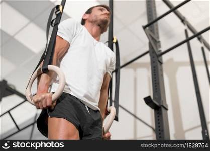 Young Male Athlete exercising With Gymnastic Rings In The Gym. High quality photo.. Young Male Athlete exercising With Gymnastic Rings In The Gym.