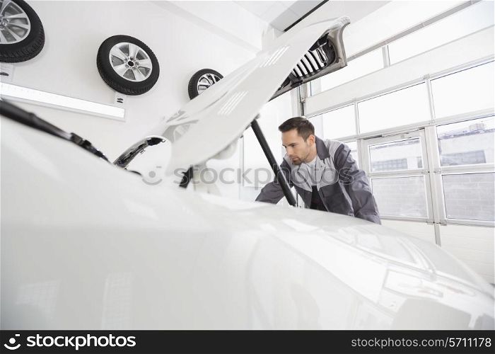 Young male automobile mechanic examining car engine in repair shop