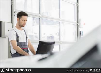 Young male automobile mechanic using computer in repair shop