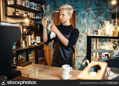 Young male barista checks clean dishes after making coffee at cafe counter. Barman works in cafeteria, bartender occupation. Barista checks clean dishes after making coffee