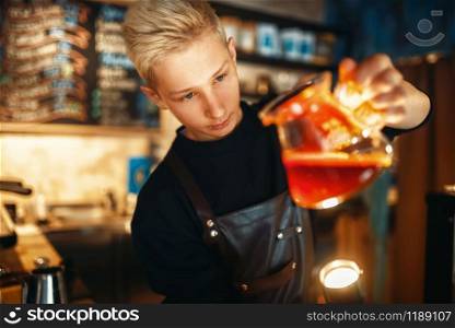 Young male barista in apron checks the sediment in the coffee pot. Barman works in cafeteria, bartender prepares espresso. Male barista checks the sediment in the coffee pot