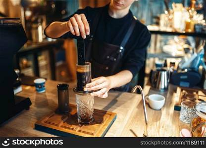 Young male barista makes fresh espresso, black coffee preparation at cafe counter. Barman works in cafeteria, bartender occupation. Young male barista makes fresh espresso in cafe