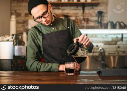 Young male barman pours coffee in a glass. Coffee house on the background.