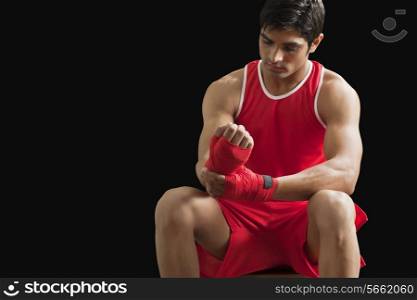 Young male boxer taping up hands against black background