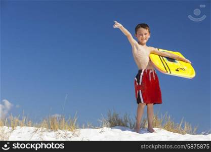 Young male boy child with yellow surfboard on a beach with bright blue sky