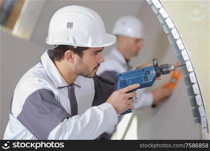 young male builder drilling the wall with drill perforator