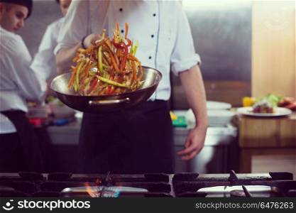 Young male chef flipping vegetables in wok at commercial kitchen. chef flipping vegetables in wok