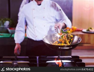 Young male chef flipping vegetables in wok at commercial kitchen. chef flipping vegetables in wok