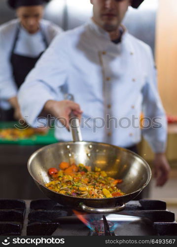 Young male chef flipping vegetables in wok at commercial kitchen. chef flipping vegetables in wok