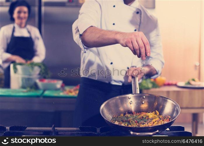 Young male chef putting spices on vegetables in wok at commercial kitchen. chef putting spices on vegetables in wok