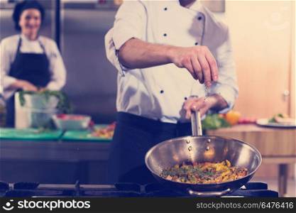 Young male chef putting spices on vegetables in wok at commercial kitchen. chef putting spices on vegetables in wok