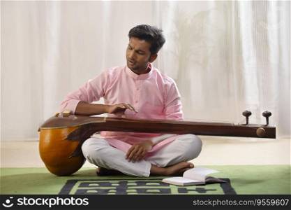 Young male classical singer playing Tanpura at home