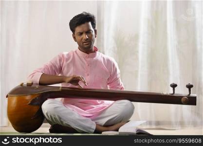 Young male classical singer playing Tanpura at home