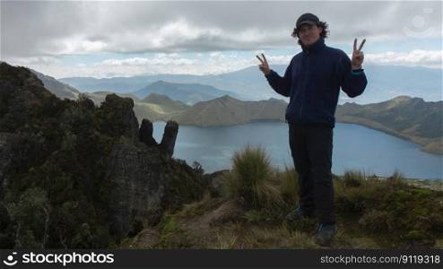 Young male climber standing on the summit of Cerro Negro next to the Mojanda lagoon wearing cap and blue coat during a cloudy day. Young male climber standing on the summit of Cerro Negro next to the Mojanda lagoon wearing cap and blue coat