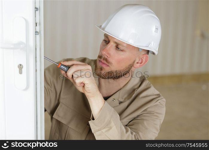 young male contractor using screwdriver on a door lock mechanism