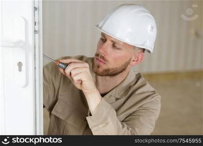 young male contractor using screwdriver on a door lock mechanism