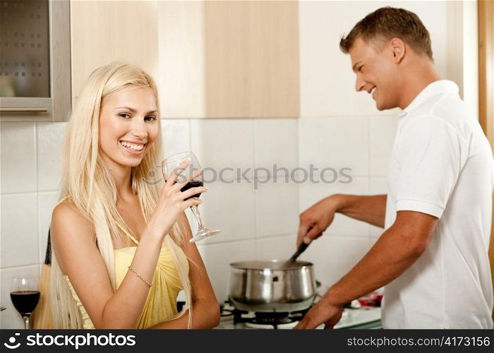 Young male cooking food while his wife enjoys wine