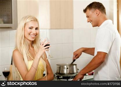 Young male cooking food while his wife enjoys wine